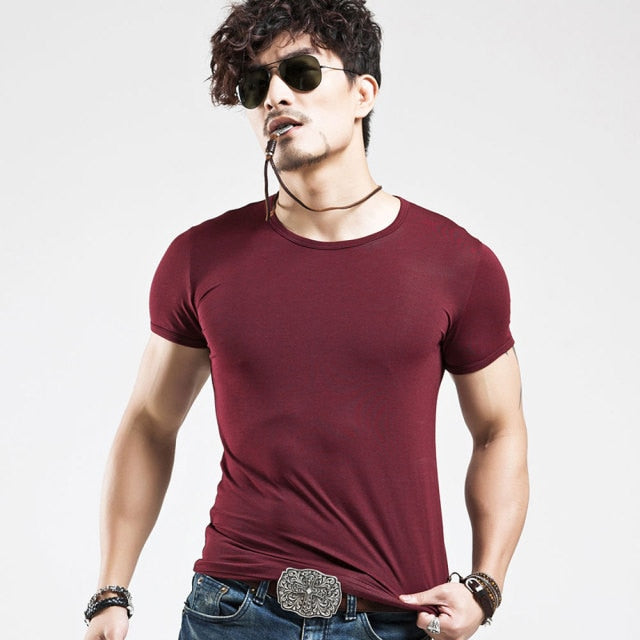 T-shirt stretch pour hommes - Mandenge - rouge bordeaux;  le mannequin est debout et porte des lunettes de soleil. Le mannequin est caucasien et a une barbe.  Il a son collier dans sa bouche et tire sur son t-shirt vers le bas.